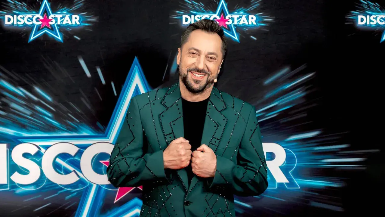 Marcin Miller w zielonej marynarce ozdobionej błyszczącymi kamieniami, uśmiecha się na tle sceny Disco Star.