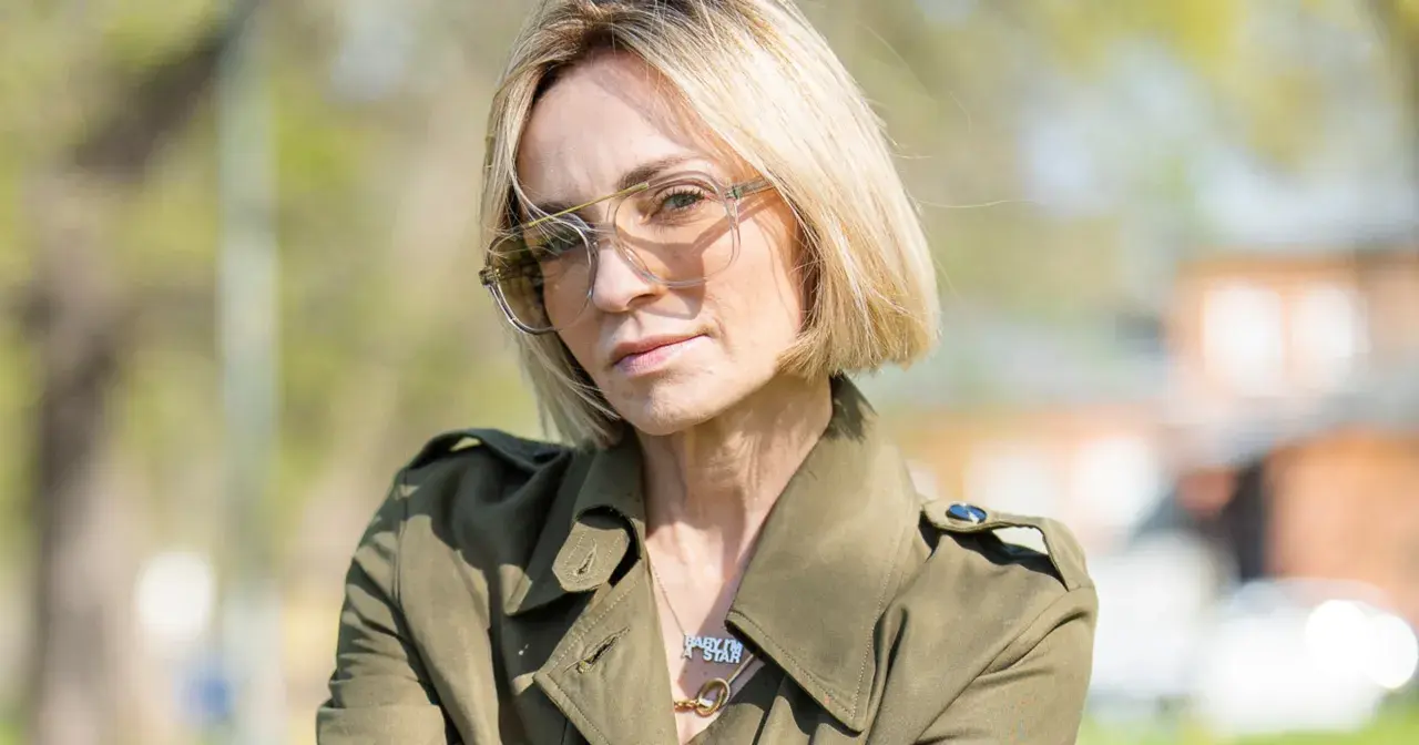 Anna Wyszkoni w okularach i zielonym płaszczu, na tle zieleni.