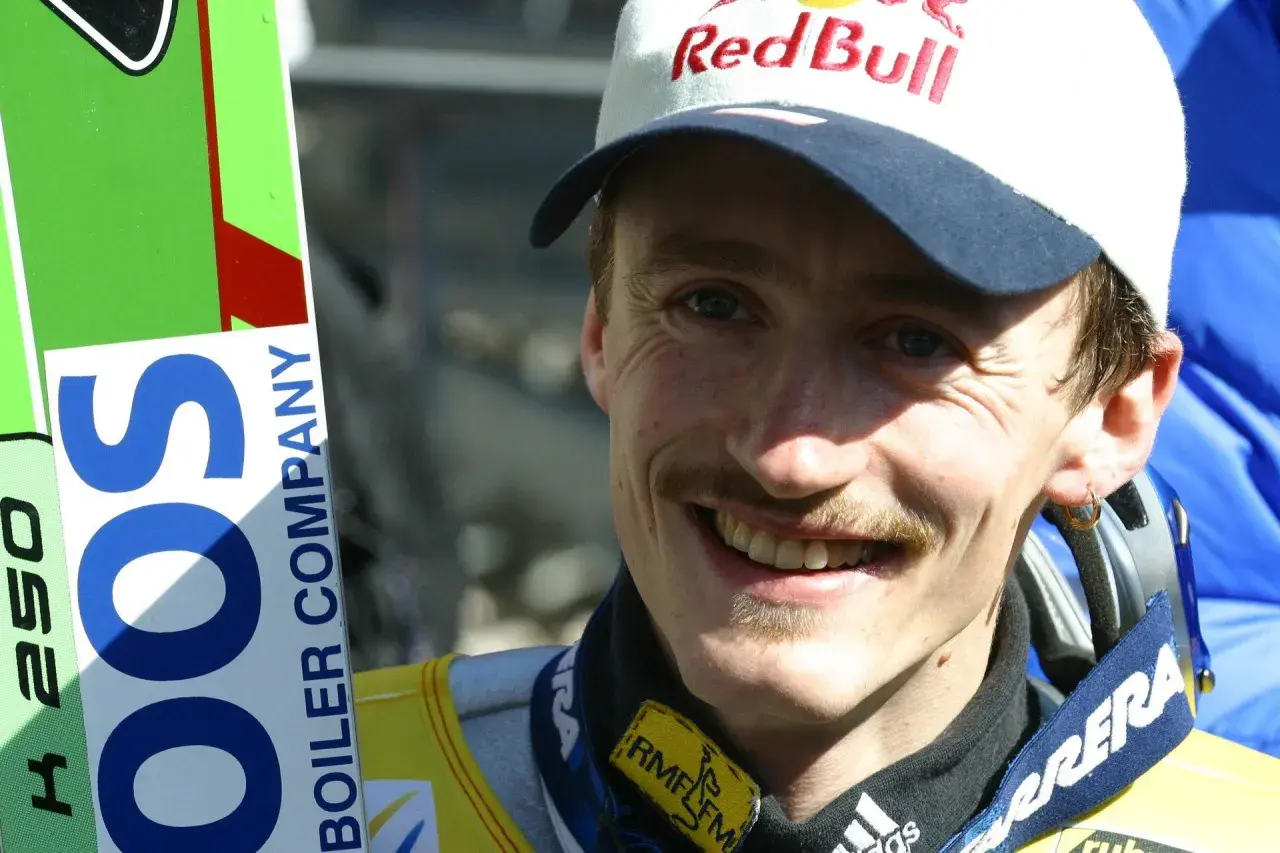 Adam Małysz w czapce Red Bull i z nartami.