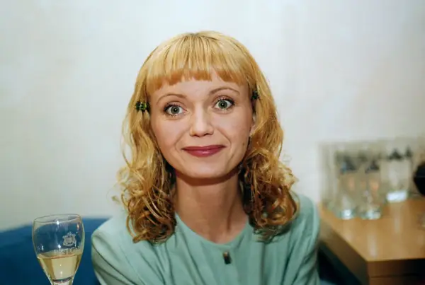 Olga Borys z blond włosami i zielonymi spinkami, w zielonej bluzce, z kieliszkiem wina.
