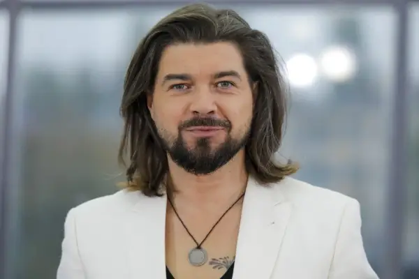 Tomasz Szczepanik w białej marynarce, z długimi włosami i brodą, patrzy w obiektyw.